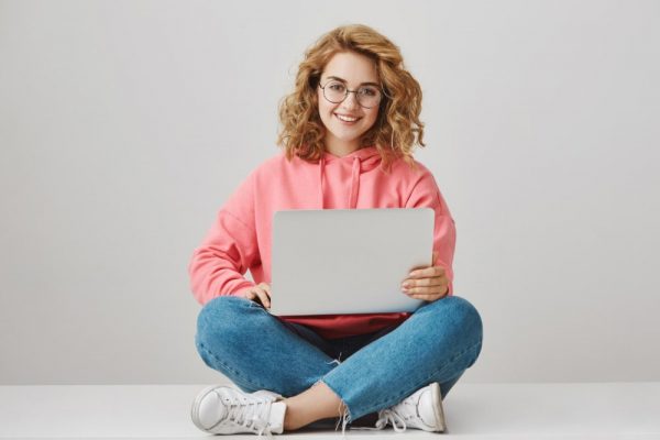 cute-freelance-girl-using-laptop-sitting-floor-smiling-min